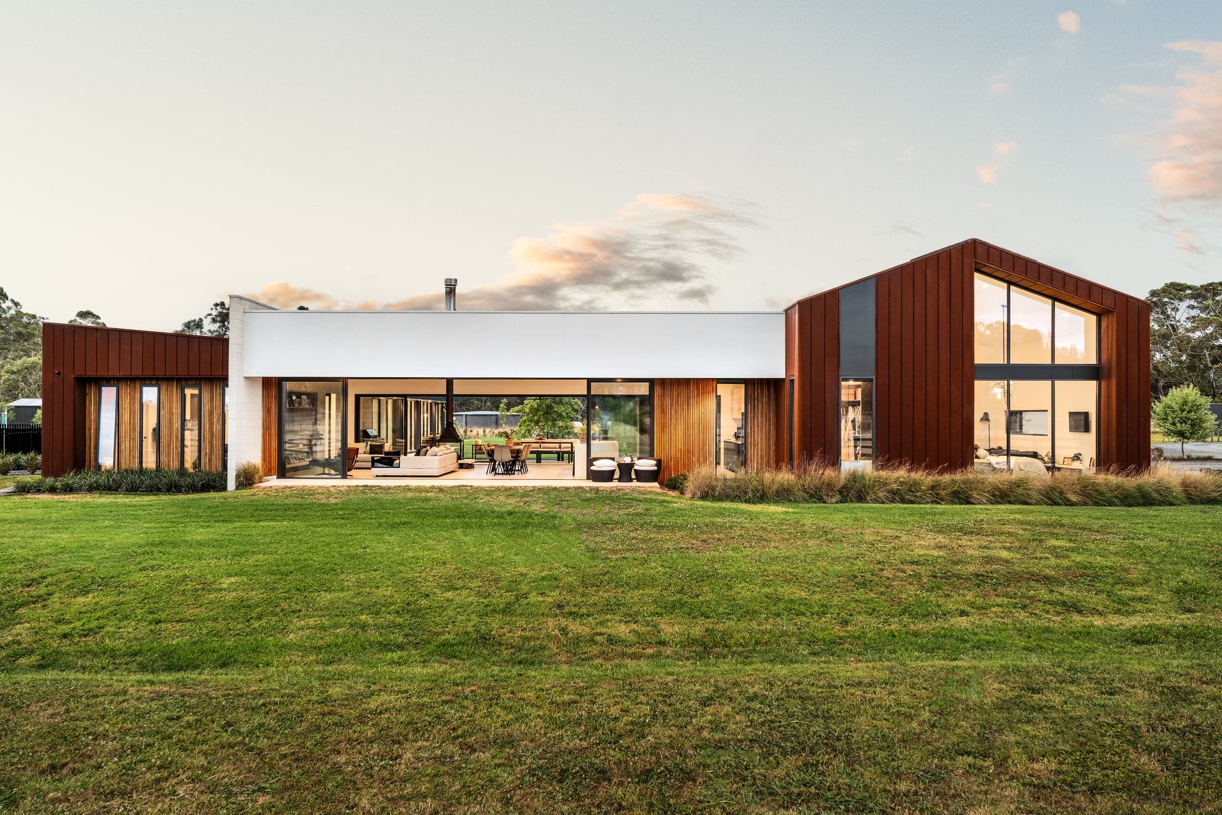 Long low facade of a rural home at dusk, lit from within, Pakenham